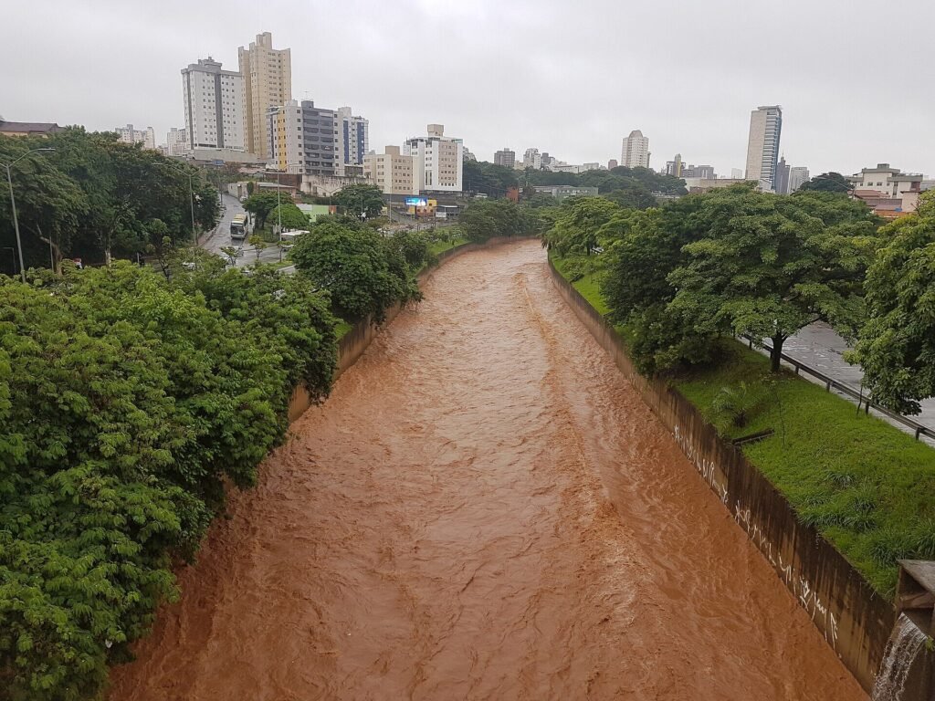 Canal cheio cercado de árvores com prédios de Belo Horizonte ao fundo