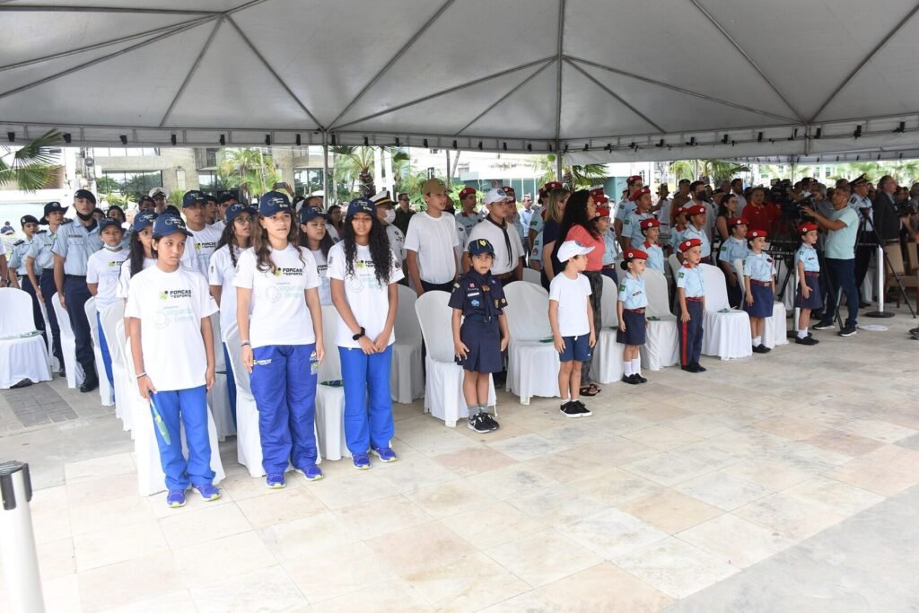 Crianças e adolescentes uniformizados em pé durante cerimônia sob tenda em Fortaleza