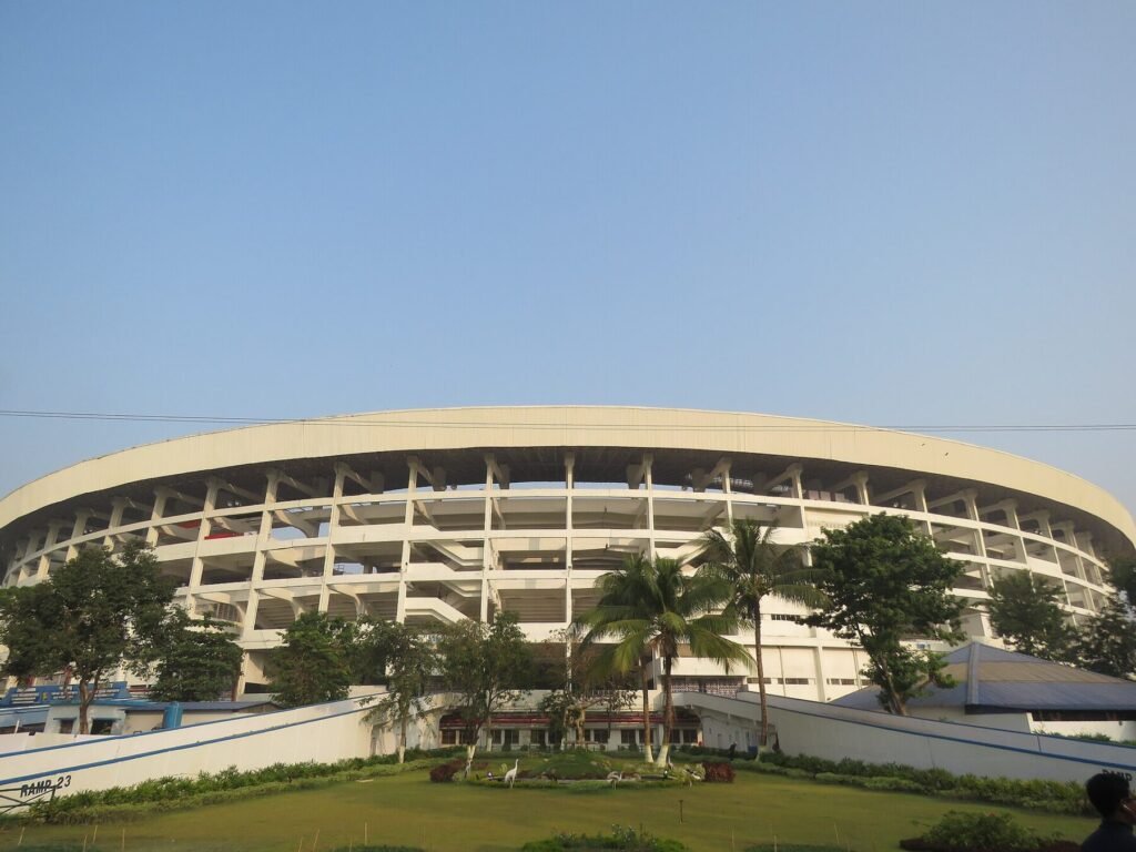Fachada circular do Salt Lake Stadium, em Calcutá, com palmeiras e jardim à frente
