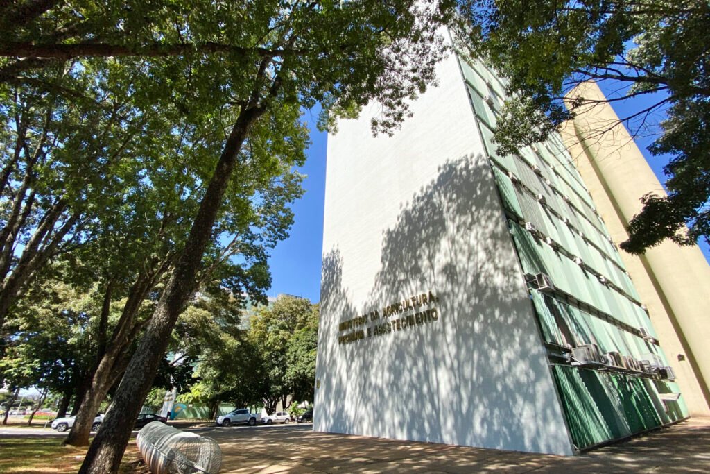 Fachada branca de prédio da Esplanada dos Ministérios entre árvores