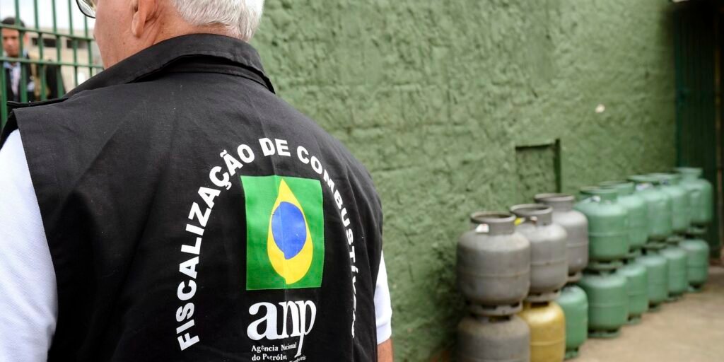 Fiscal com colete da ANP de costas, ao lado de botijões de gás empilhados