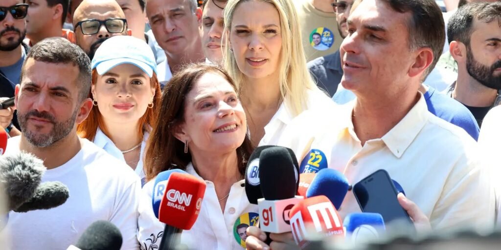 Flávio Bolsonaro cercado de apoiadores e microfones
