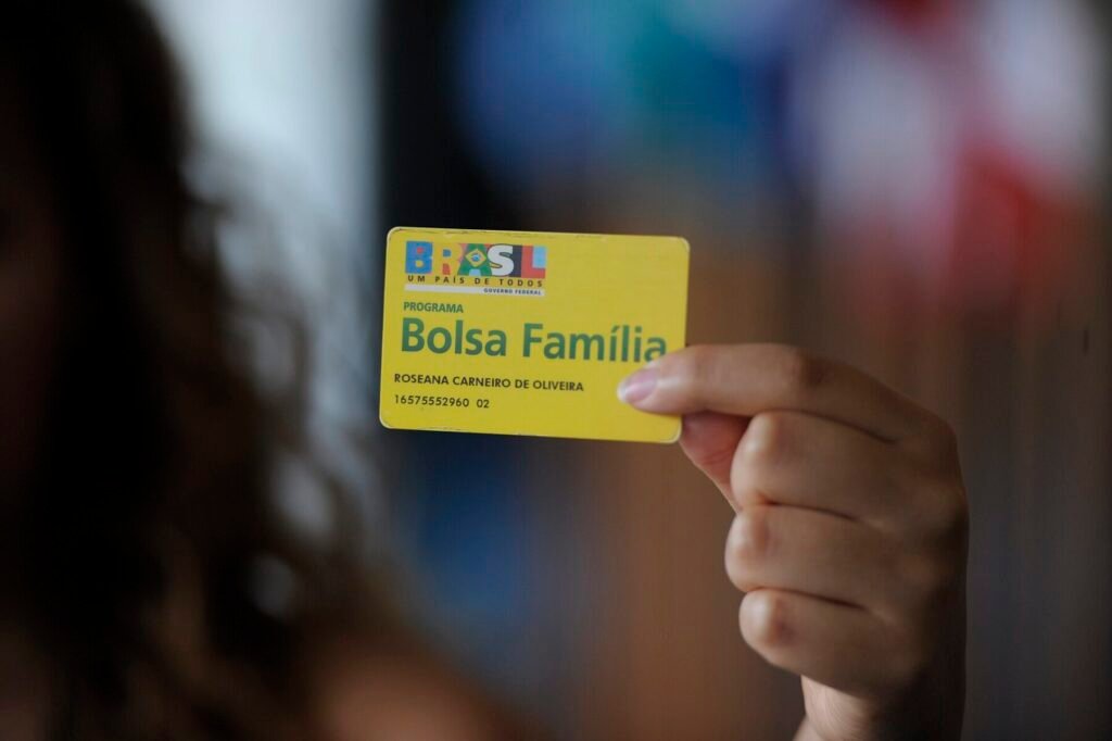 Mão segura cartão amarelo do Bolsa Família
