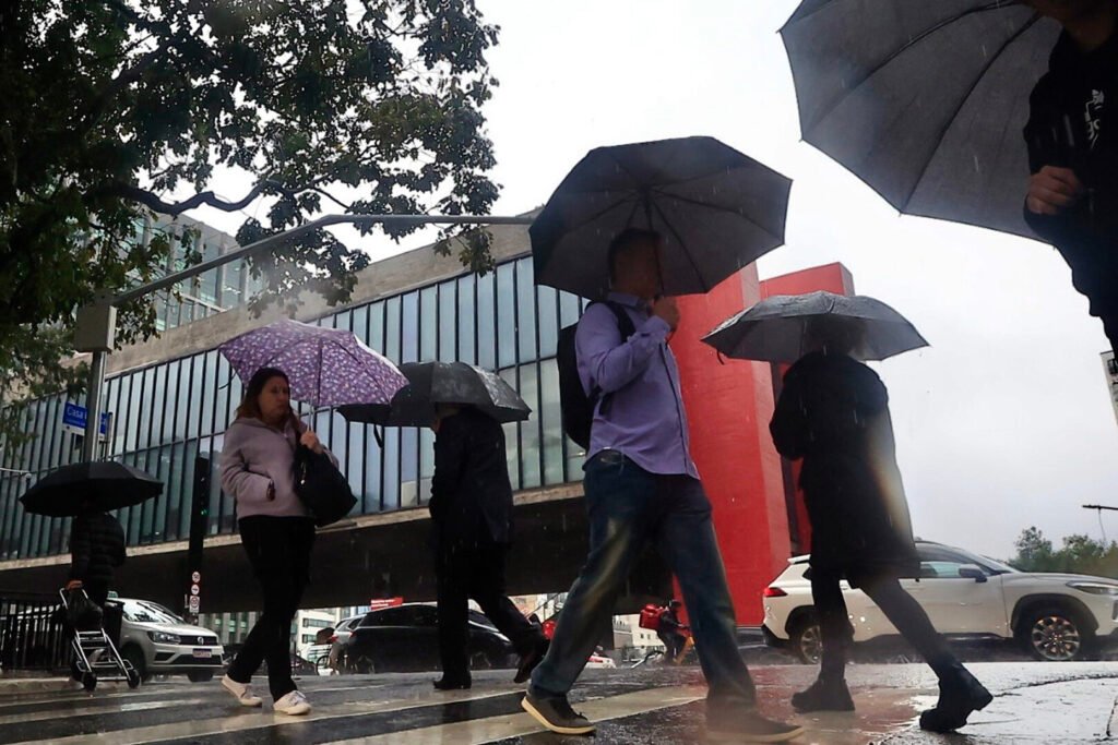Pessoas caminham com guarda-chuvas sob chuva em São Paulo