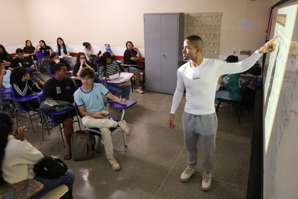 Professor aponta para o quadro diante de alunos em sala de aula